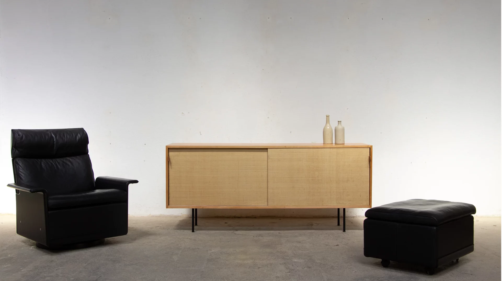 Ensemble Lounge Chair RZ 62 Dieter Rams Vitsoe cuir noir swivel et son ottoman devant une Knoll 116 sideboard en raphia